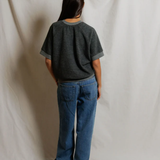 Person wearing a dark gray t-shirt and blue jeans standing against a plain white background