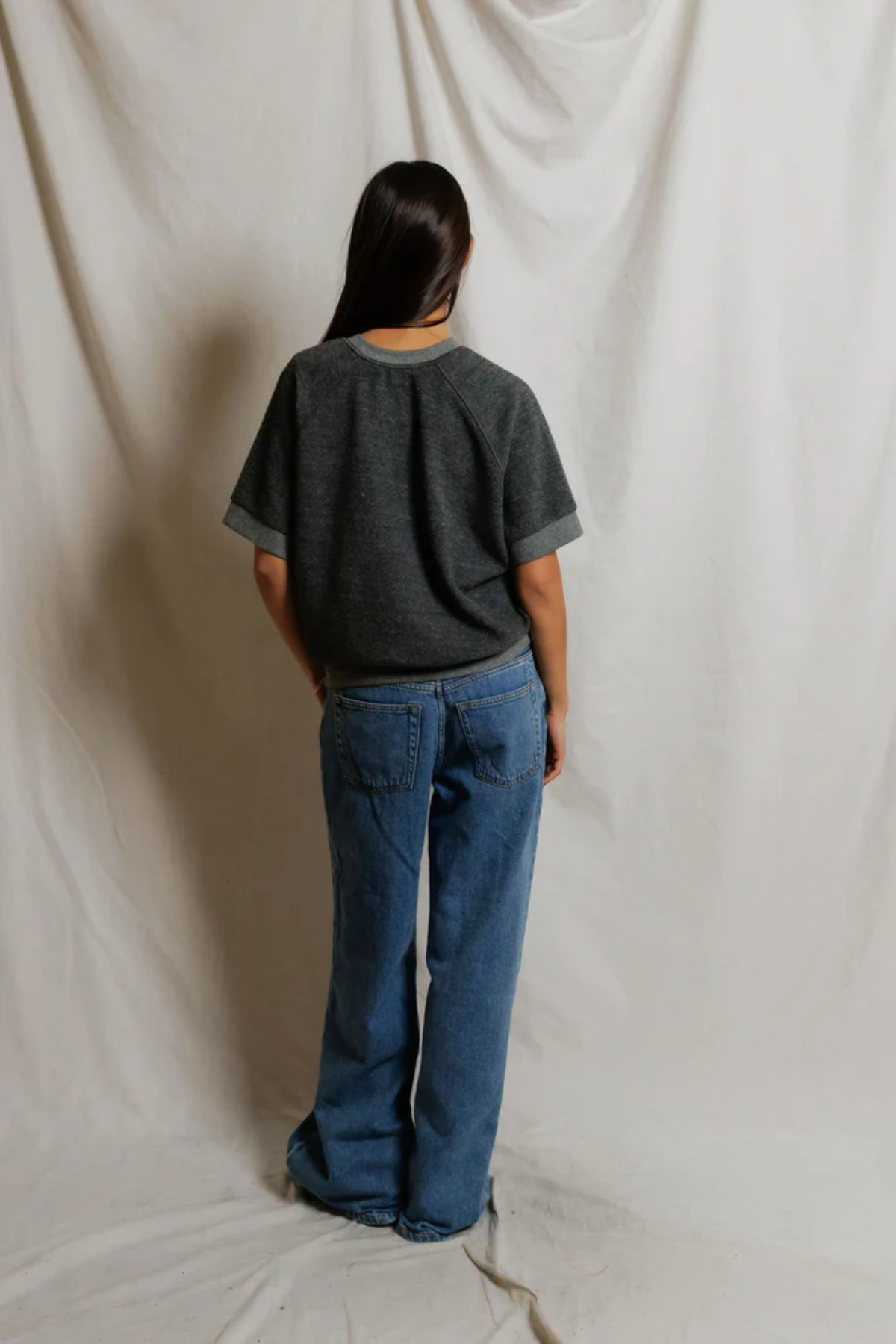 Person wearing a dark gray t-shirt and blue jeans standing against a plain white background