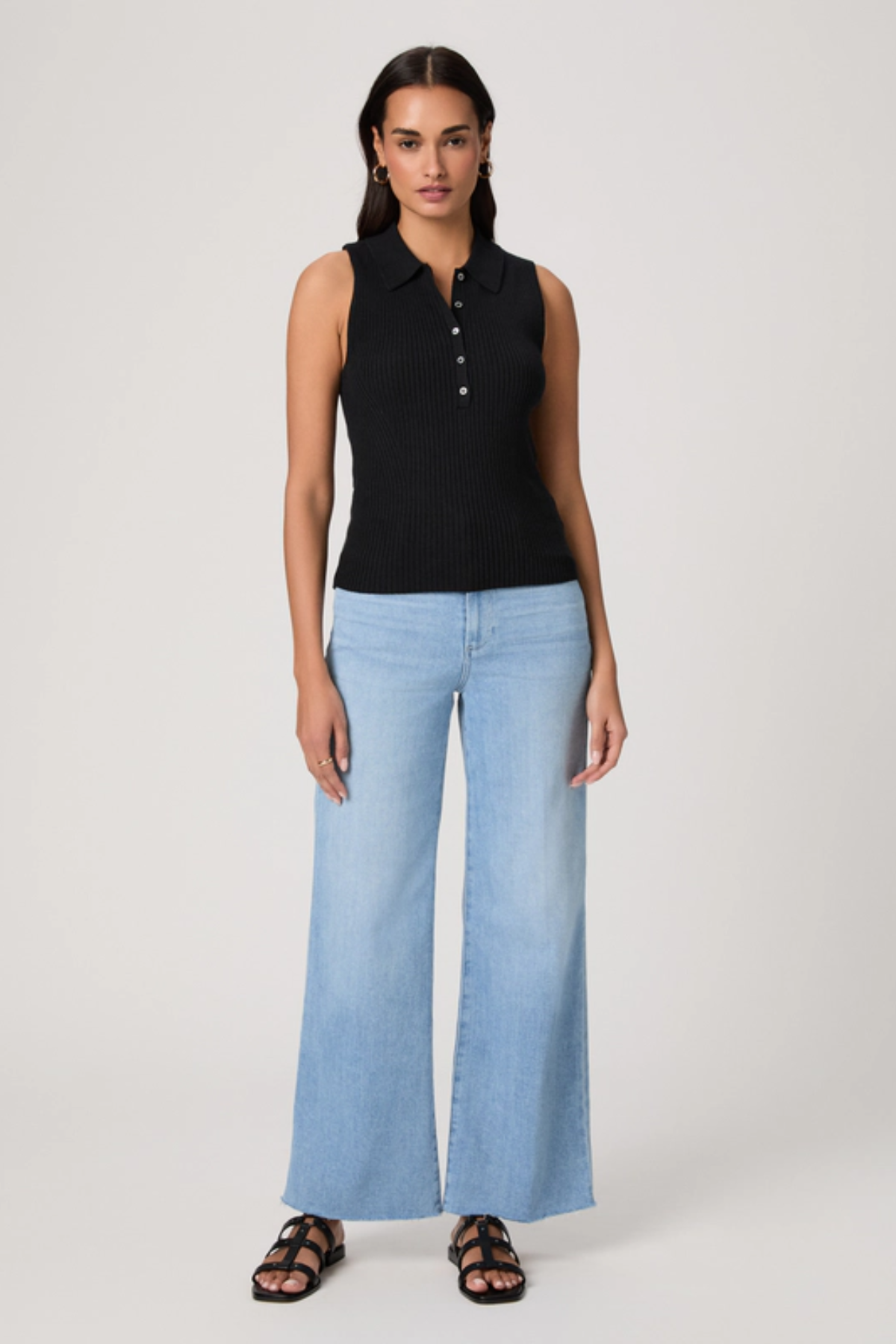 Woman wearing a black sleeveless top and light blue jeans on a white background