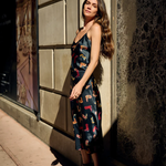 Woman in a patterned dress standing against a textured wall.