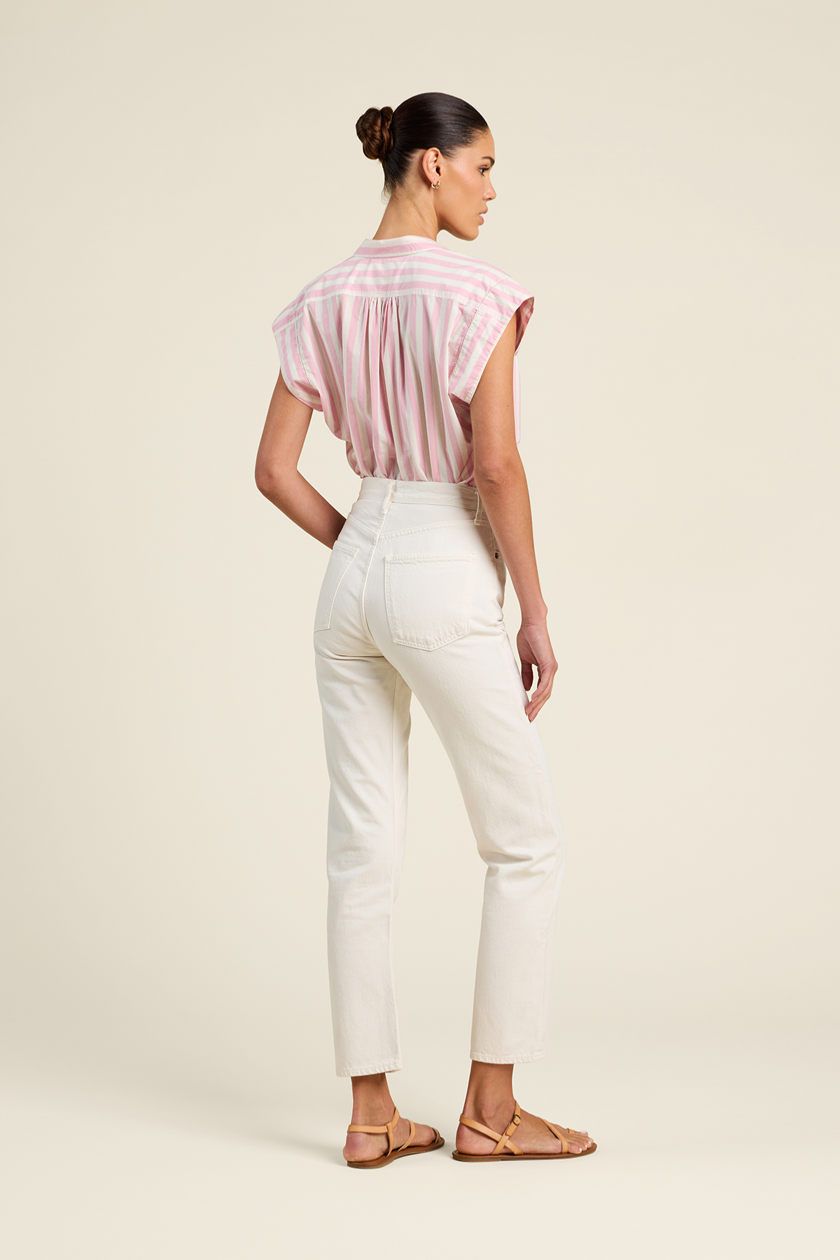 Woman wearing a pink blouse and white pants on a beige background