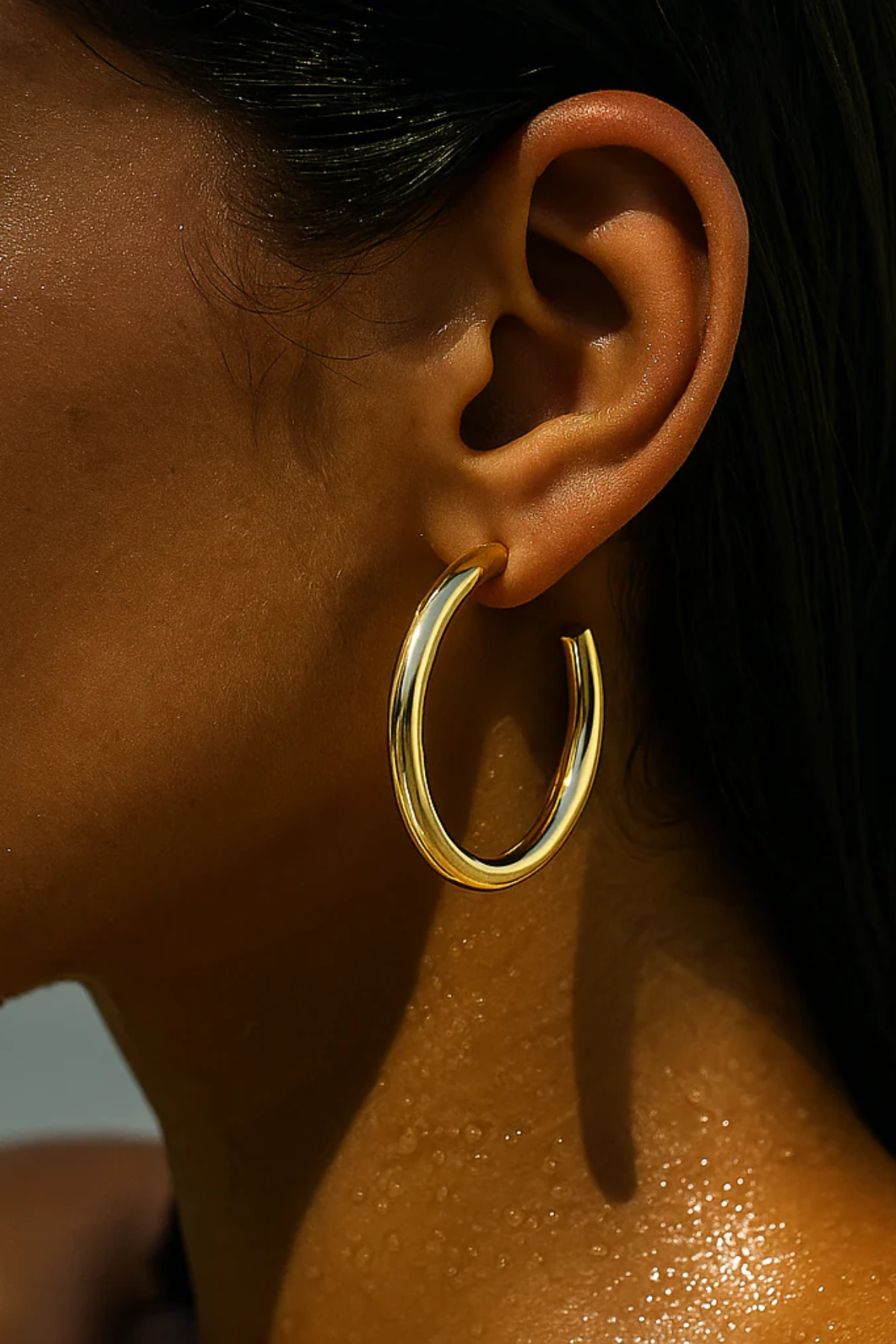Close-up of an ear wearing a gold hoop earring with a blurred background