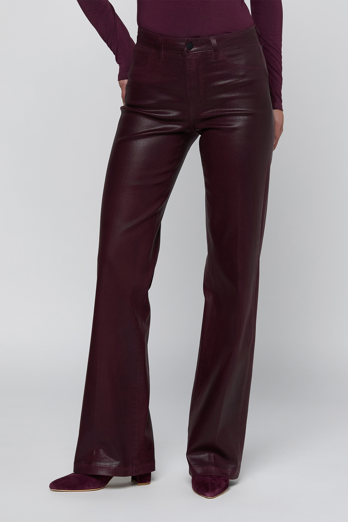 A model wearing high-waisted, wide-leg faux leather pants in a deep burgundy color, paired with a matching long-sleeve top and pointed-toe heels, against a light gray studio background.