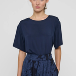 A woman modeling a navy blue short-sleeve top with a matching navy floral lace skirt against a light gray studio background.