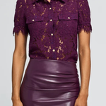 A woman wearing a short-sleeve purple lace button-up shirt with puff sleeves and a shiny purple faux-leather pencil skirt, shown from the nose down against a light gray studio background.