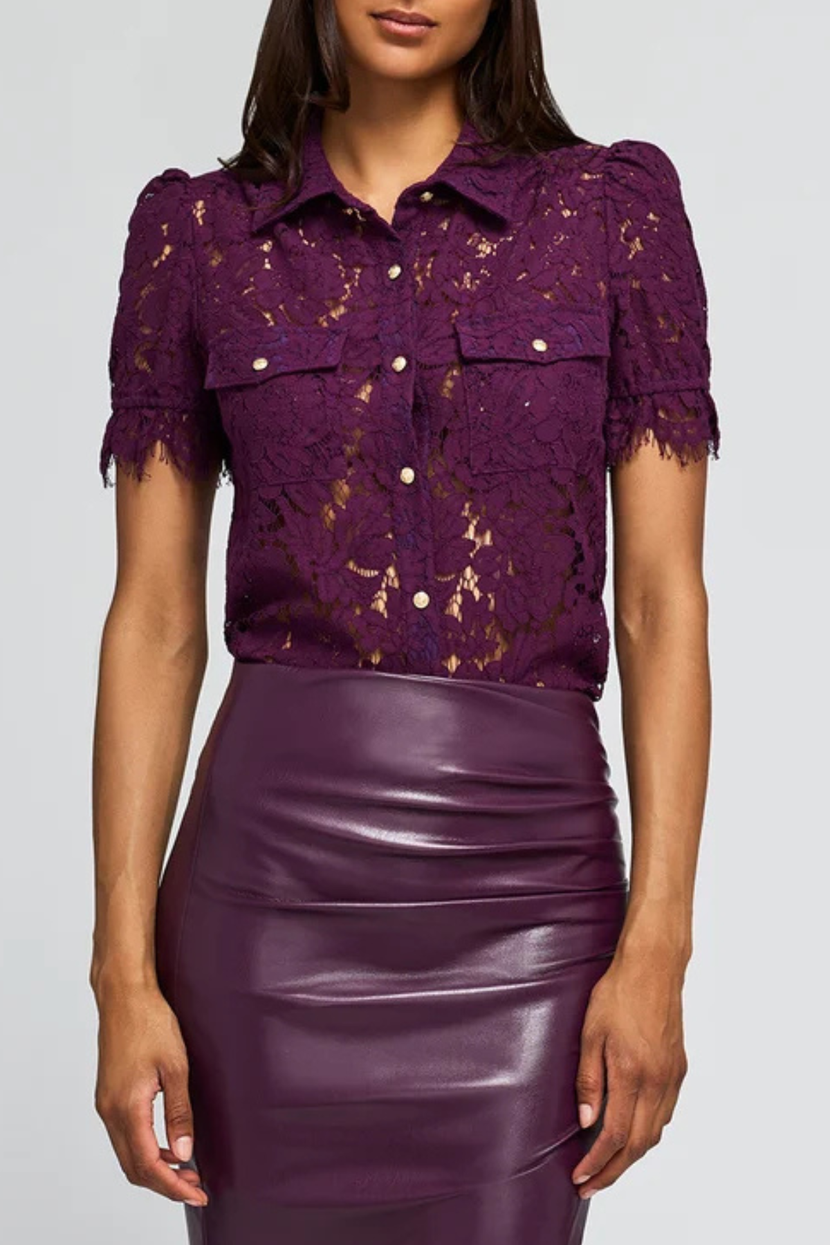 A woman wearing a short-sleeve purple lace button-up shirt with puff sleeves and a shiny purple faux-leather pencil skirt, shown from the nose down against a light gray studio background.