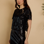 Woman wearing a black lace top and black leather skirt against a beige background