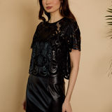 Woman wearing a black lace top and black leather skirt against a beige background