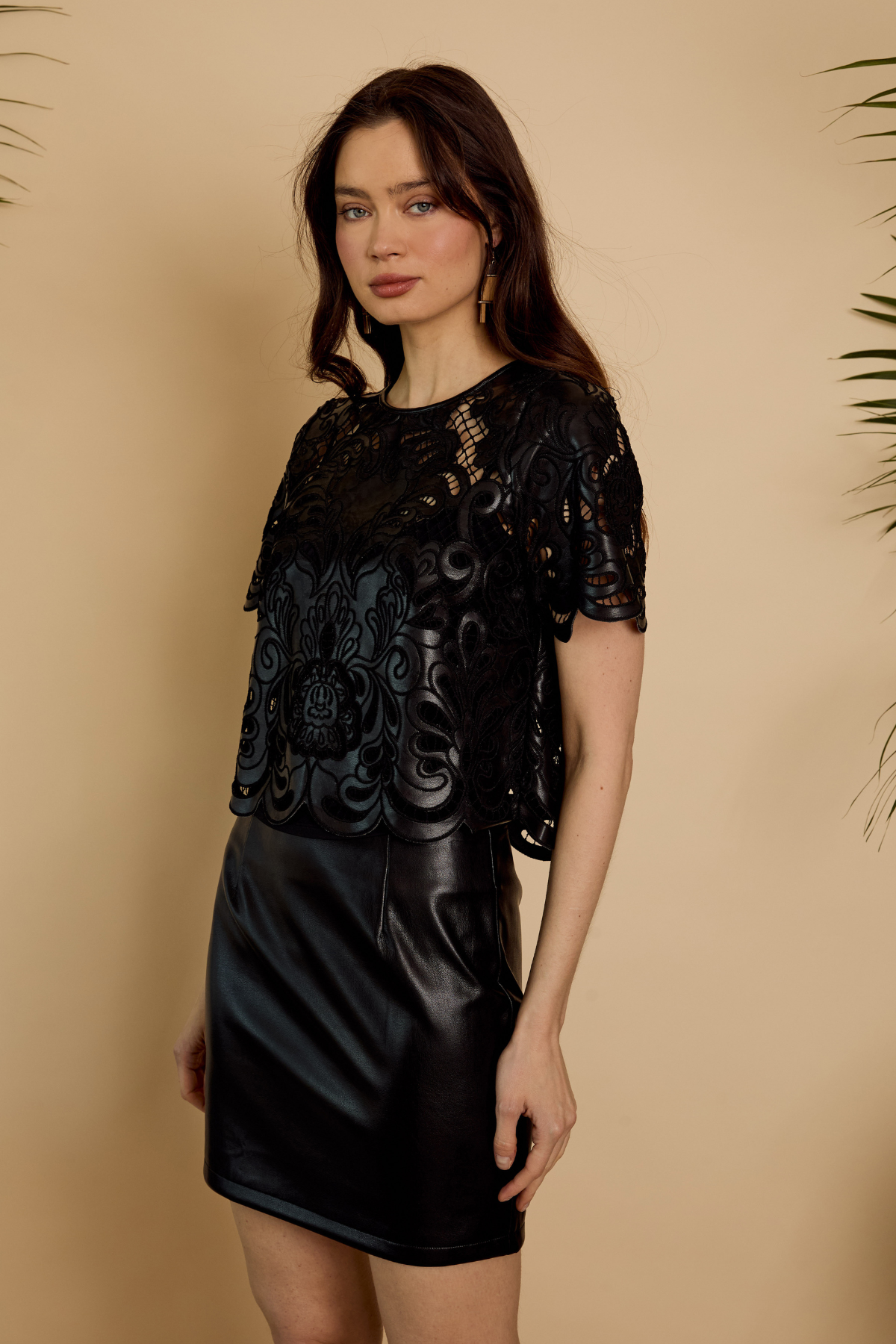 Woman wearing a black lace top and black leather skirt against a beige background