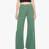 A model wearing a pair of sage green wide-leg denim pants with a black mesh crop top and gray heeled sandals, photographed against a plain white studio background.