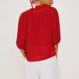 Person wearing a red top and white shorts with a patterned headscarf on a plain background