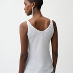 Woman wearing a white tank top and blue jeans on a plain background