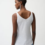 Woman wearing a white tank top and blue jeans on a plain background