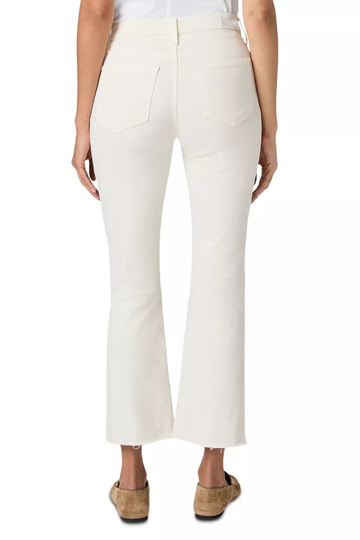 A person shown from the back wearing off-white cropped flare jeans with a white top and tan flat shoes, photographed against a plain white studio background.
