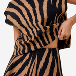 A close-up of a model wearing a matching two-piece knit set with a bold black and tan tiger-stripe pattern. The set includes a high-neck, short-sleeved top and a matching flared skirt.