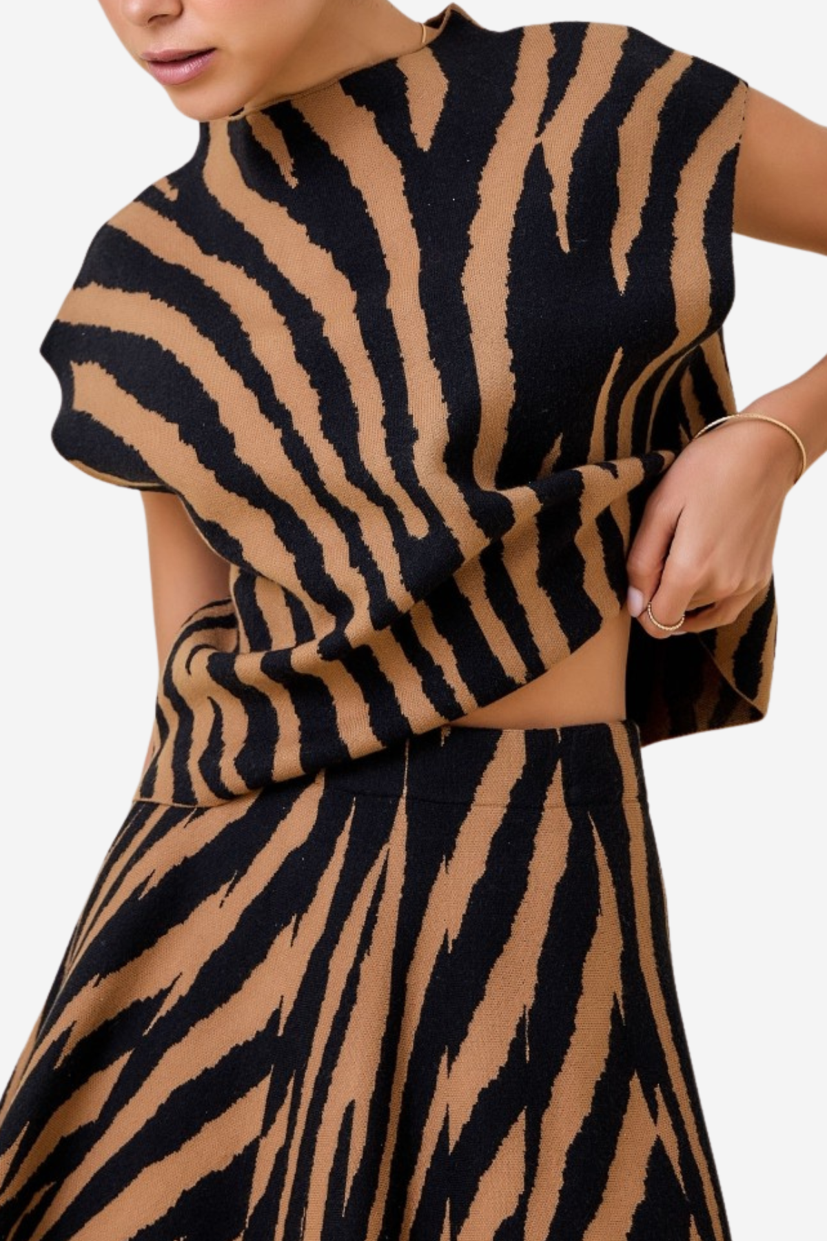 A close-up of a model wearing a matching two-piece knit set with a bold black and tan tiger-stripe pattern. The set includes a high-neck, short-sleeved top and a matching flared skirt.
