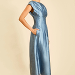 A woman modeling a light blue satin midi dress with cap sleeves and side pockets, standing against a solid beige background.