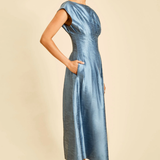 A woman modeling a light blue satin midi dress with cap sleeves and side pockets, standing against a solid beige background.