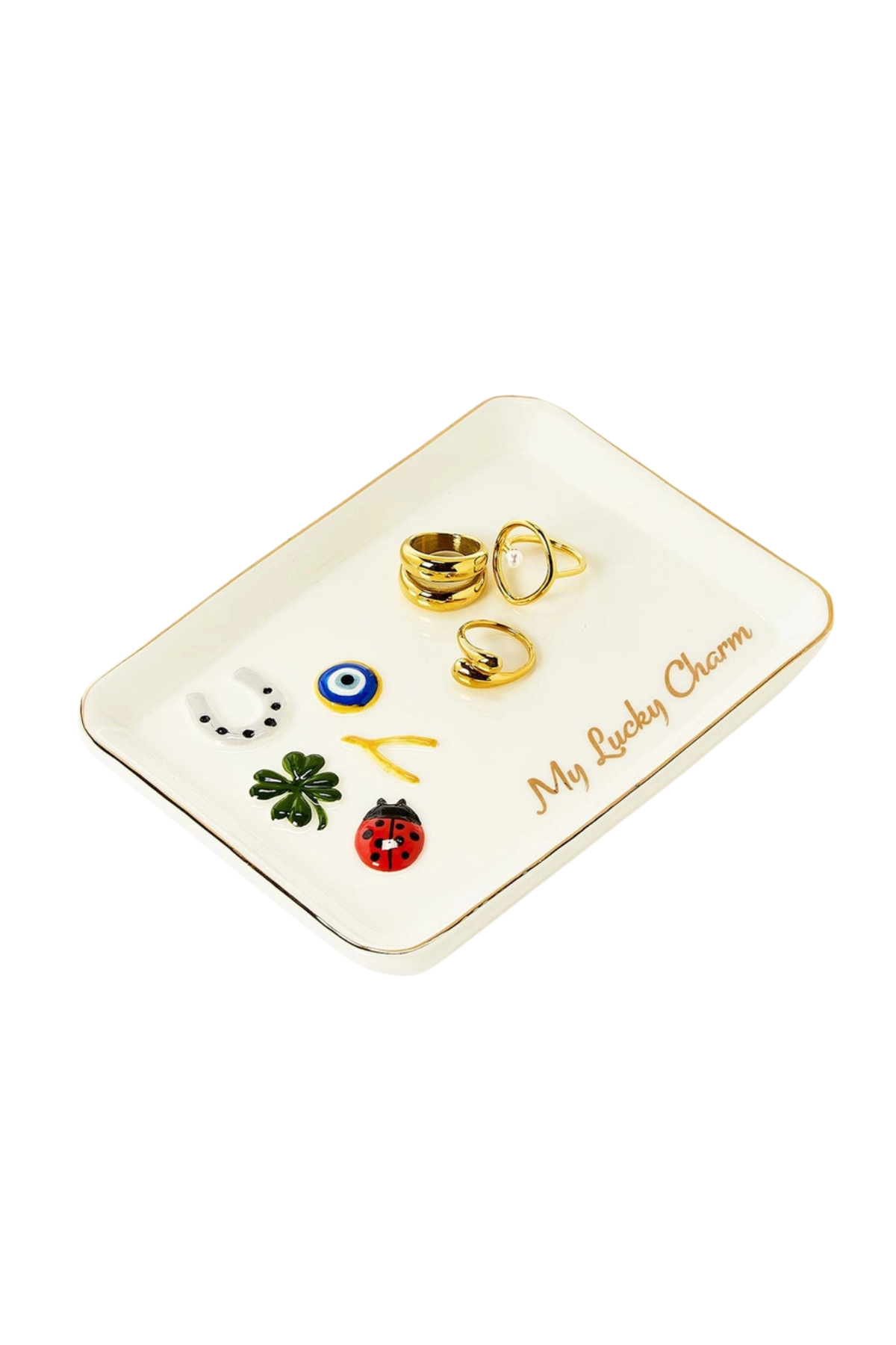 A white ceramic jewelry organizer tray with gold trim, featuring the text 'My Lucky Charm' and displaying several small charms, including a green four-leaf clover, a red ladybug, a blue and white evil eye, and gold rings, on a solid white background.
