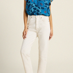woman in blue floral blouse and white pants on tan background 