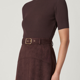 Woman wearing a brown ribbed knit top and matching skirt with a belt on a white background