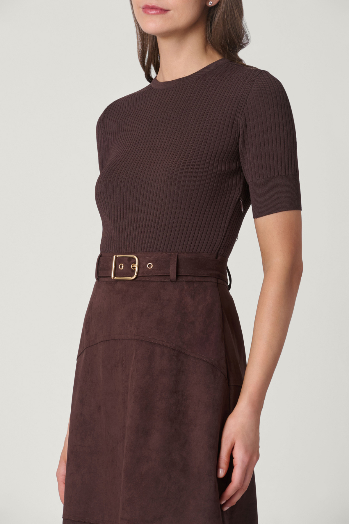 Woman wearing a brown ribbed knit top and matching skirt with a belt on a white background