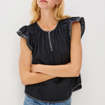 Woman wearing a black top with ruffled sleeves and blue jeans against a white background
