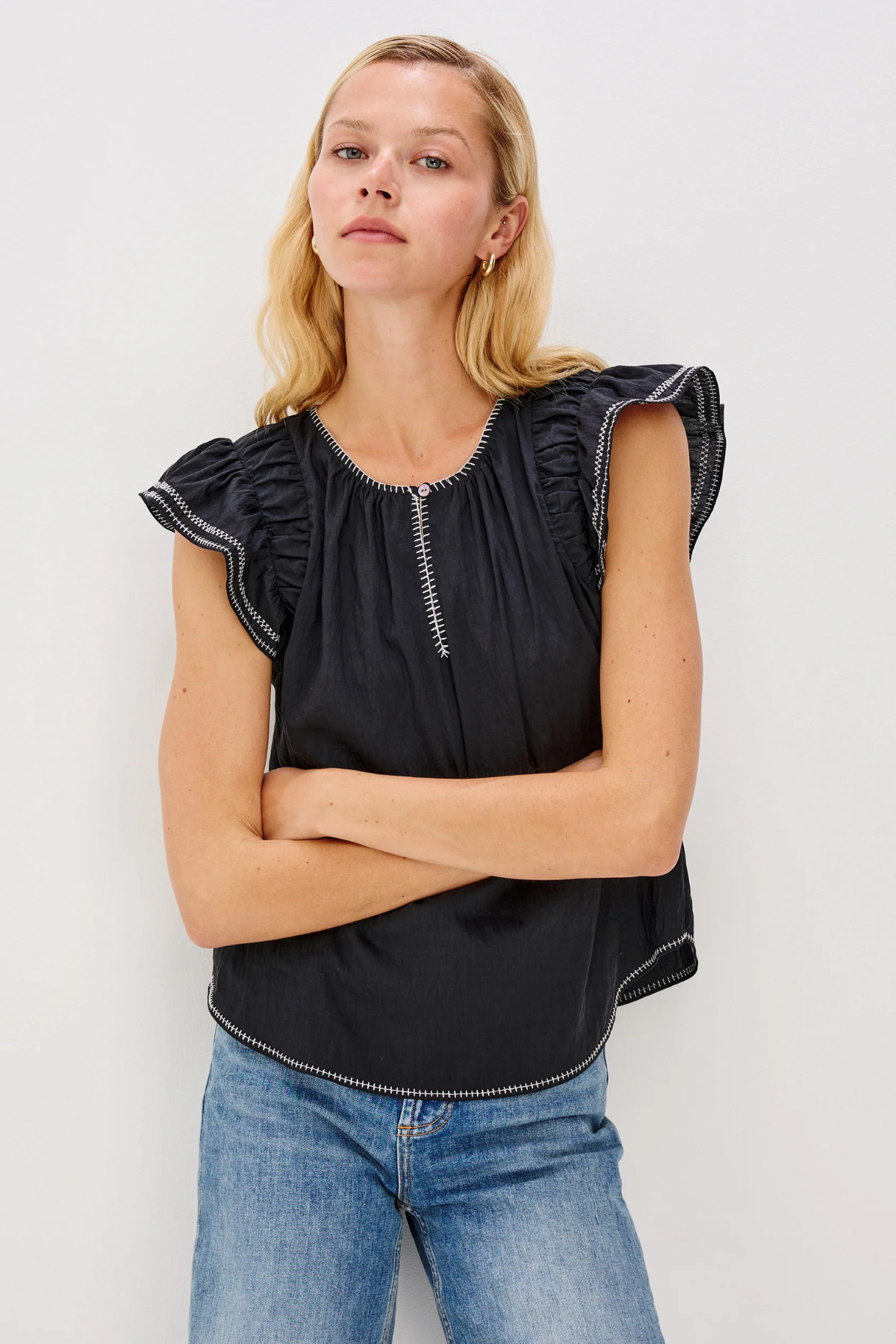 Woman wearing a black top with ruffled sleeves and blue jeans against a white background