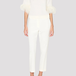 A model wearing a white mock-neck knit top with feathered elbow-length sleeves and matching white cropped trousers, paired with white pointed-toe heels, against a solid light gray background.
