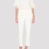 A model wearing a white mock-neck knit top with feathered elbow-length sleeves and matching white cropped trousers, paired with white pointed-toe heels, against a solid light gray background.