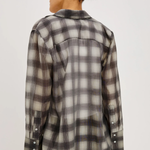 A woman shown from the back wearing a long-sleeve plaid button-up shirt in gray, black, and off-white, paired with black pants against a light gray studio background.