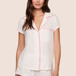 Woman wearing a white pajama set with pink piping on a beige background