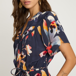 Woman wearing a navy dress with colorful floral pattern on a plain background