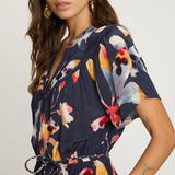 Woman wearing a navy dress with colorful floral pattern on a plain background