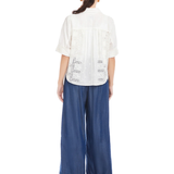 Woman wearing a white blouse with lace details and blue wide-leg pants on a white background