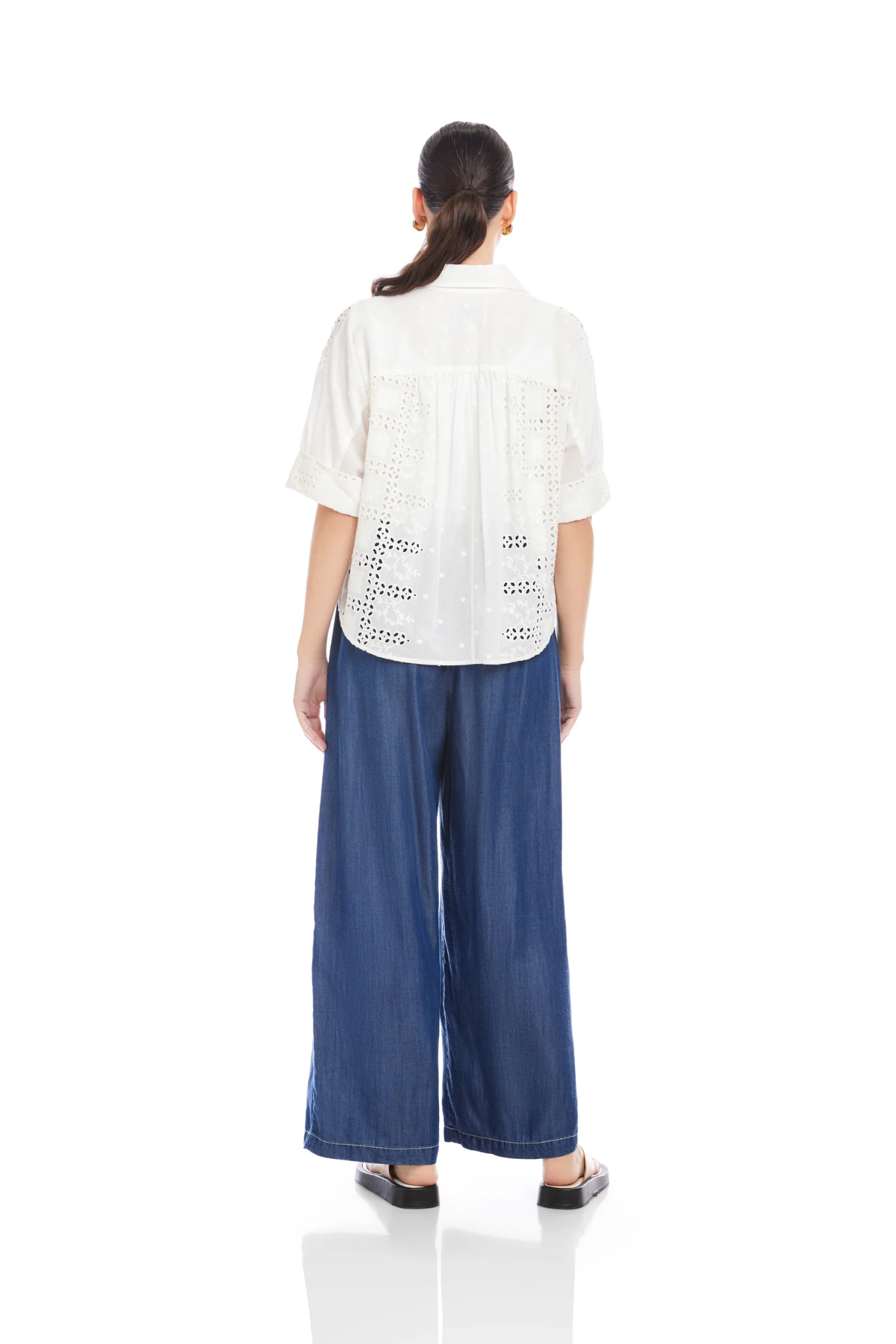 Woman wearing a white blouse with lace details and blue wide-leg pants on a white background