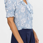 Woman wearing a light blue floral blouse with a deep neckline and navy shorts on a white background