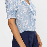 Woman wearing a light blue floral blouse with a deep neckline and navy shorts on a white background