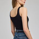 A woman shown from the back wearing a black ribbed tank top and blue jeans against a light gray studio background.