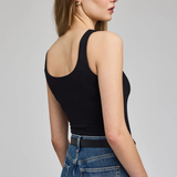 A woman shown from the back wearing a black ribbed tank top and blue jeans against a light gray studio background.