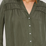 An olive green long-sleeve blouse with a V-neckline, button-up front, and delicate shoulder pleats, shown on a model.