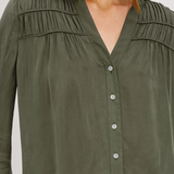 An olive green long-sleeve blouse with a V-neckline, button-up front, and delicate shoulder pleats, shown on a model.
