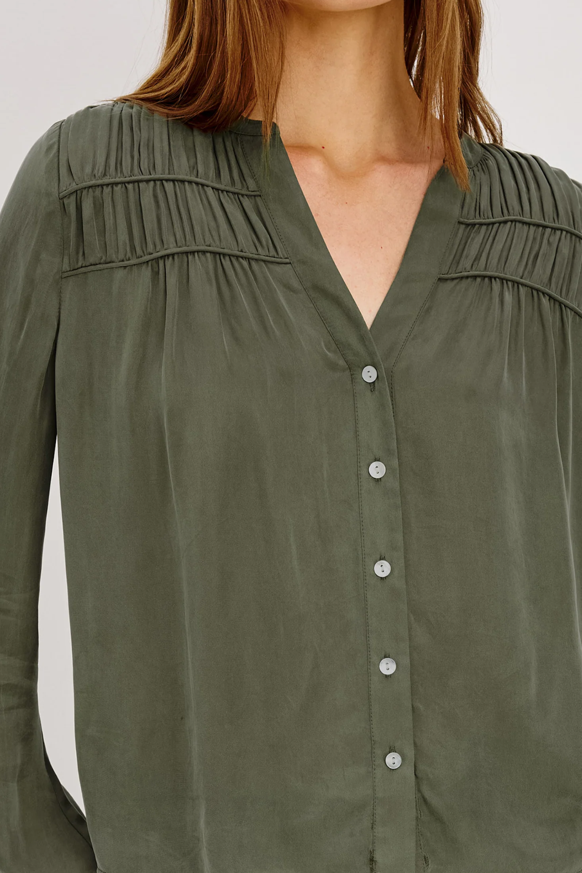 An olive green long-sleeve blouse with a V-neckline, button-up front, and delicate shoulder pleats, shown on a model.