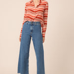 Woman wearing a red and white patterned blouse with blue jeans on a beige background