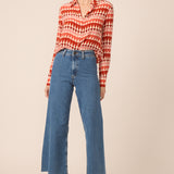 Woman wearing a red and white patterned blouse with blue jeans on a beige background