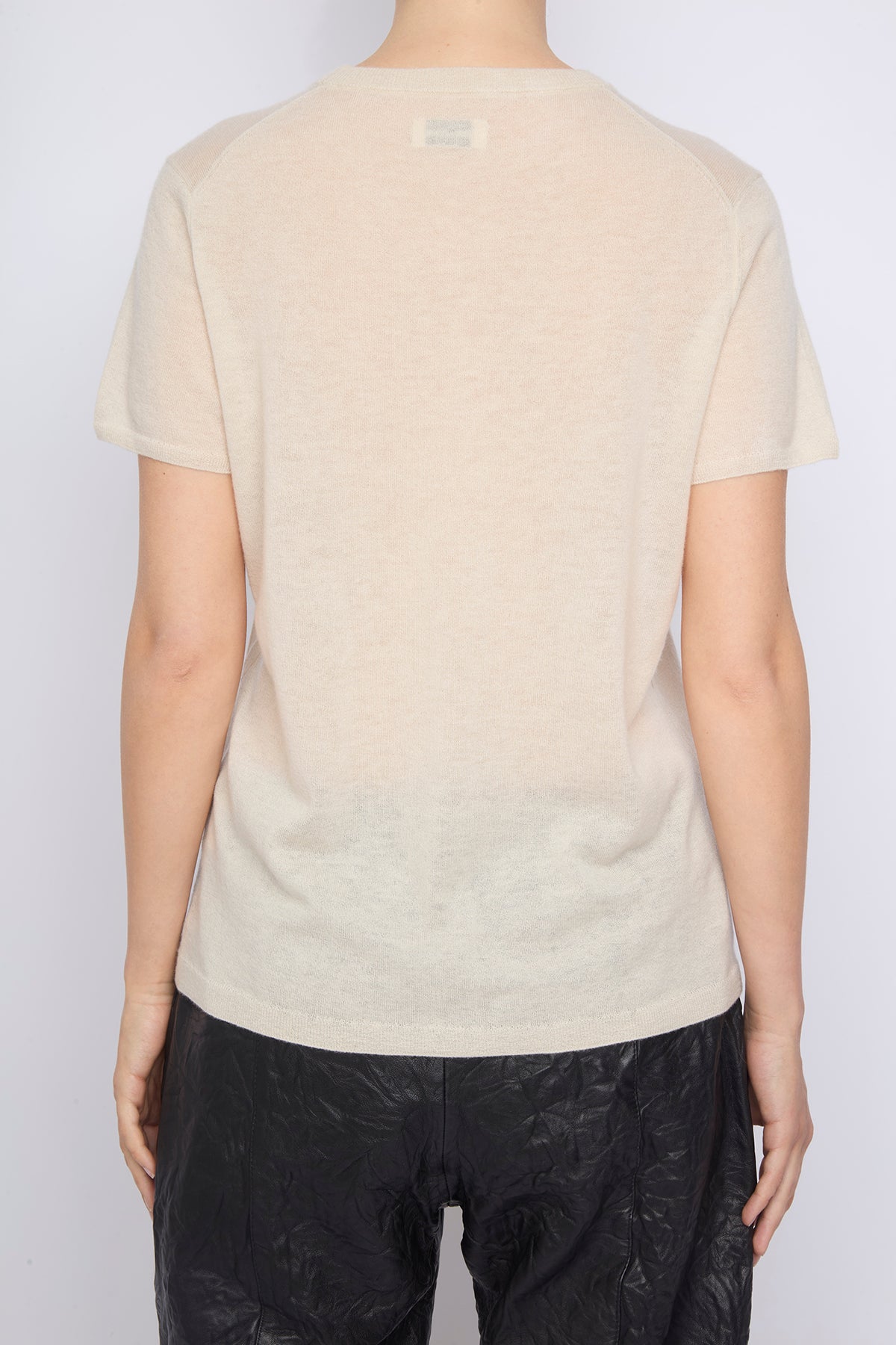 Person wearing a beige t-shirt with a subtle pattern on a plain background