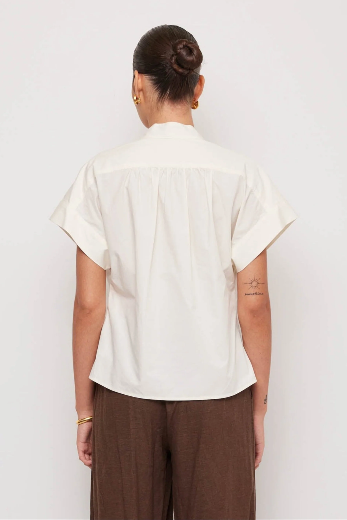 Person wearing a white shirt and brown pants against a white background