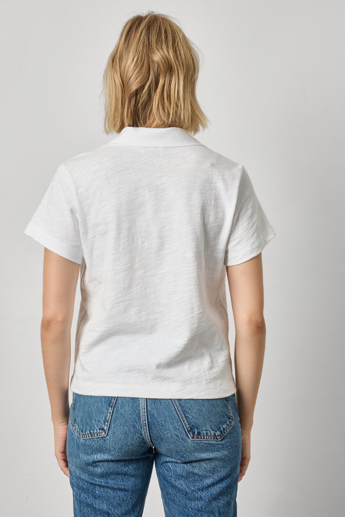 Person wearing a white polo shirt and blue jeans on a plain background