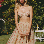 Woman in a floral dress and bikini top standing outdoors with greenery in the background