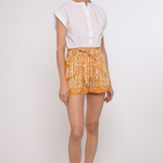 Model wearing tailored tan shorts and white cotton top with a clean, relaxed silhouette.